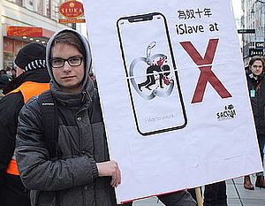 Ein Südwind Aktivist macht mit einem Schild auf die miserablen Arbeitsbedingungen beim Konzern Apple aufmerksam