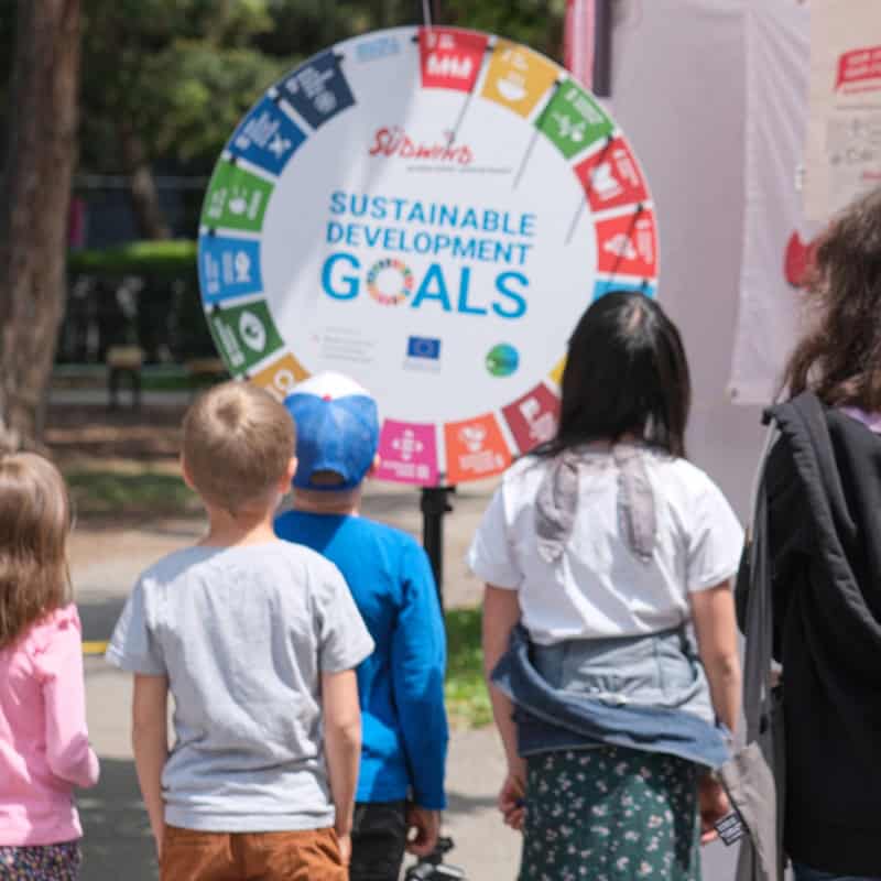 Kinder stehen vor einem Glücksrad auf dem die SDGs aufgezeichnet sind