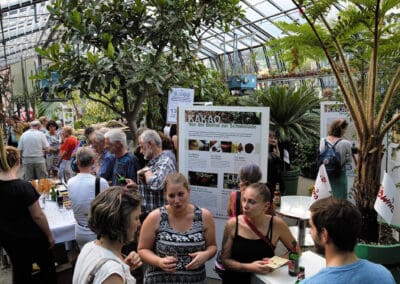 Eine große Gruppe von Menschen bewegen sich zwischen Ausstellungsplakaten und Pflanzen in einem großen Raum