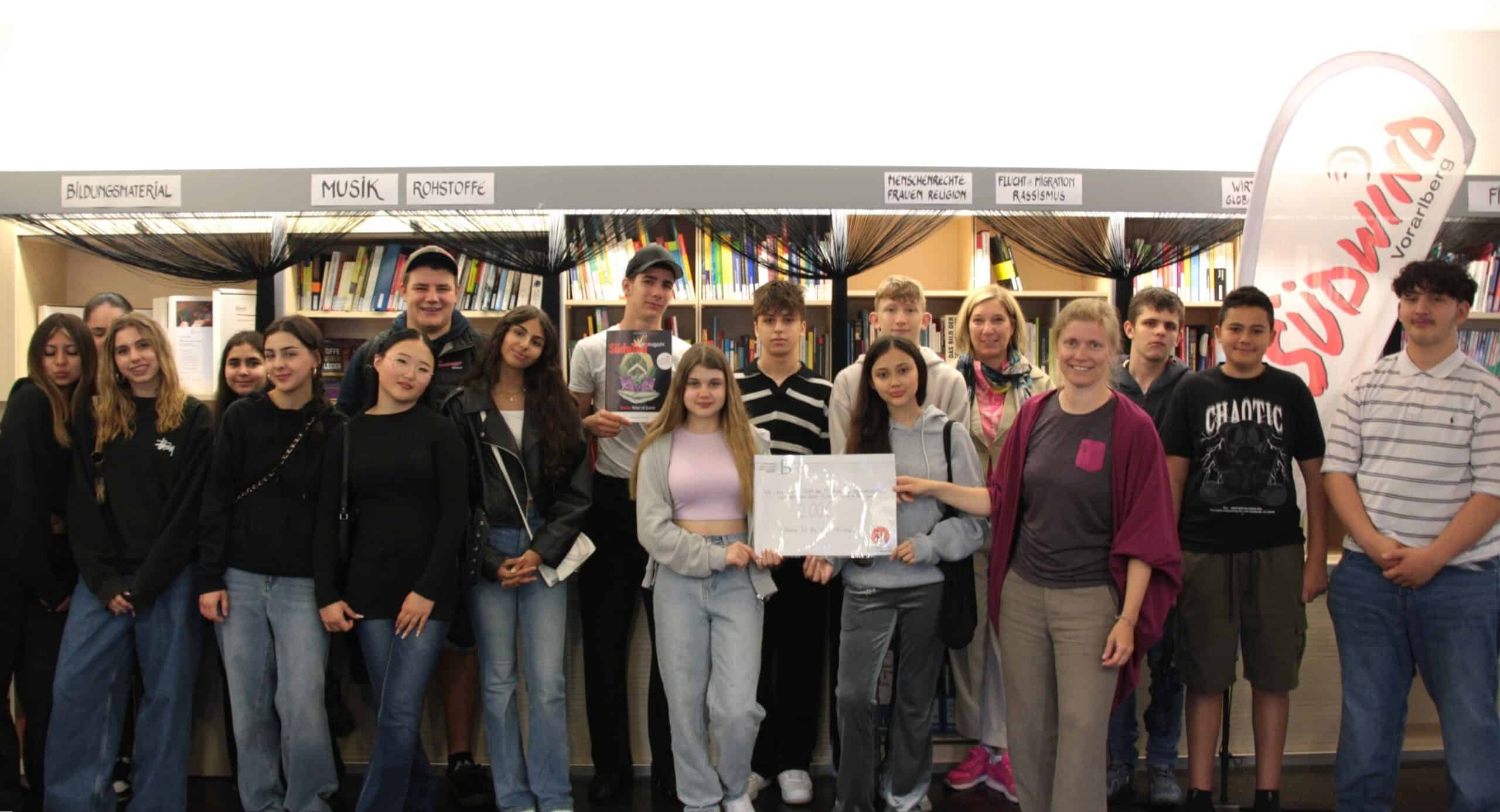 Gruppe Schülerinnen posiert vor Bücherregalen der Südwind Bibliothek in Vorarlberg